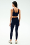 A woman stands with her back to the camera, wearing SPLITS59's Sprint High Waist Rigor 7/8 leggings in Indigo and a matching navy sports bra, paired with white sneakers against a plain light background.
