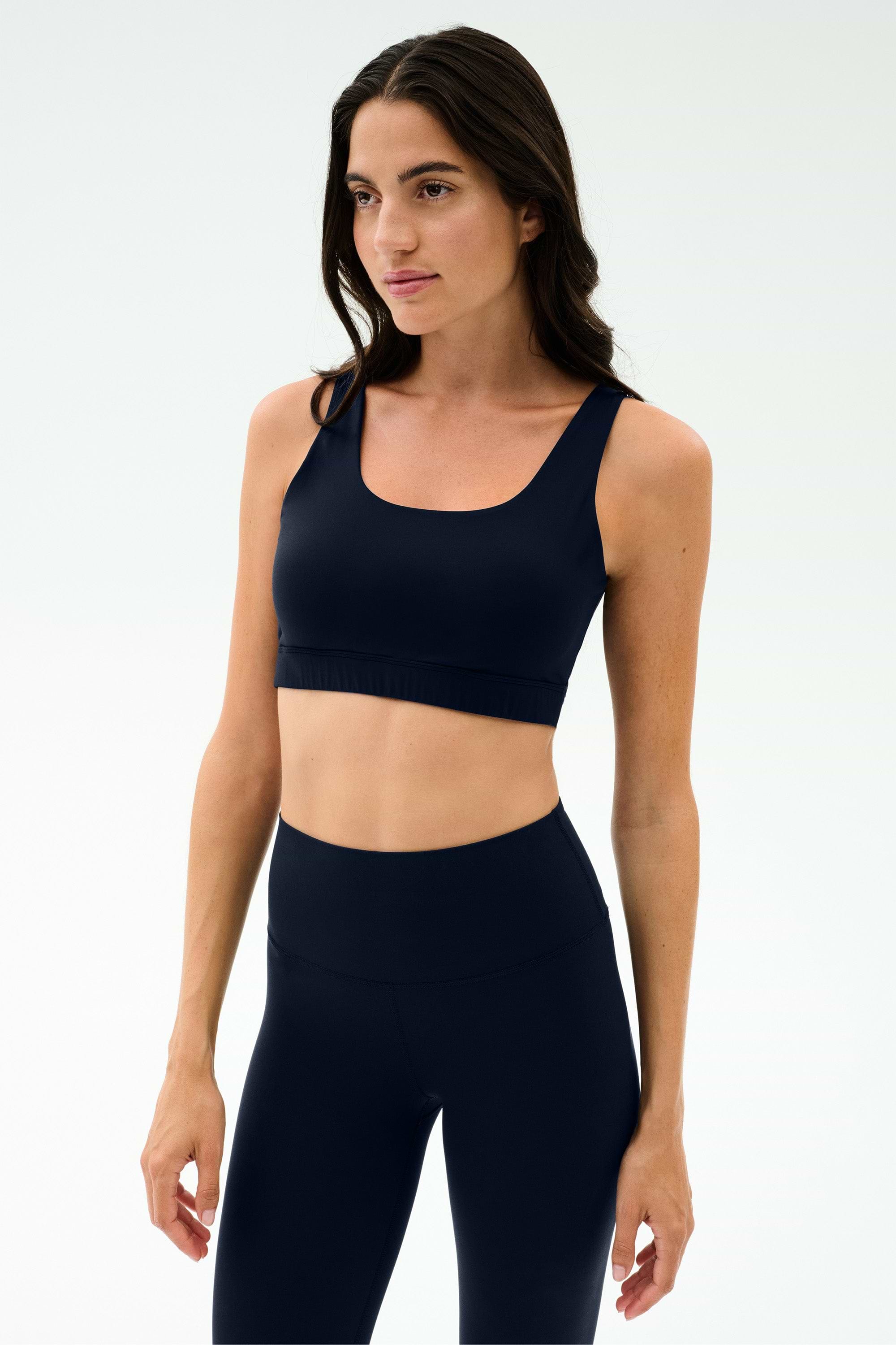 A woman wears the SPLITS59 Sprint Rigor Bralette in Indigo with high-waisted leggings, standing against a plain light background.