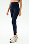 A person wearing SPLITS59 Sprint High Waist Rigor 7/8 leggings in Indigo and white athletic shoes stands against a plain light background.