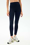 A person wearing SPLITS59 Sprint High Waist Rigor 7/8 leggings in Indigo with white athletic shoes stands against a plain light background.
