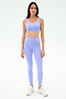 A woman stands facing forward in the SPLITS59 Sprint Rigor Bra - Purple Haze and matching leggings with white athletic shoes, designed for multi-sport performance, against a plain white background.