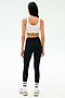 A woman, seen from behind, wears the SPLITS59 Sprint Rigor Bra in White, black high-waisted leggings, white socks, and sneakers—poised for a workout against a plain light background.