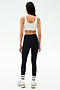 A woman, seen from behind, wears the SPLITS59 Sprint Rigor Bra in White, black high-waisted leggings, white socks, and sneakers—poised for a workout against a plain light background.
