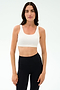 A woman wears the SPLITS59 Sprint Rigor Bra - White with black high-waisted leggings, standing against a plain white background, ready for gym workouts and multisport performance.