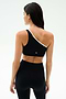 A woman faces away, wearing the SPLITS59 Josie Airweight One Shoulder Bra in Black/White with matching high-waisted leggings, set against a plain light background.