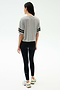A woman faces away, wearing the SPLITS59 Ava Jersey Tee in Heather Grey/Black, paired with black leggings and white sneakers, set against a plain light background.