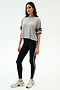 A woman stands against a plain background wearing the SPLITS59 Ava Jersey Tee in Heather Grey/Black, paired with black leggings with a white side stripe and white sneakers, ready for her gym workout.