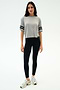 A woman poses against a white backdrop in the SPLITS59 Ava Jersey Tee - Heather Grey/Black, styled with black leggings and white athletic shoes—ideal for workouts or running.