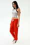 A woman stands against a white background wearing the SPLITS59 Kiki Rib Crop Tank in Heather Grey/Black, bright red drawstring sweatpants, and white sneakers with black detailing.