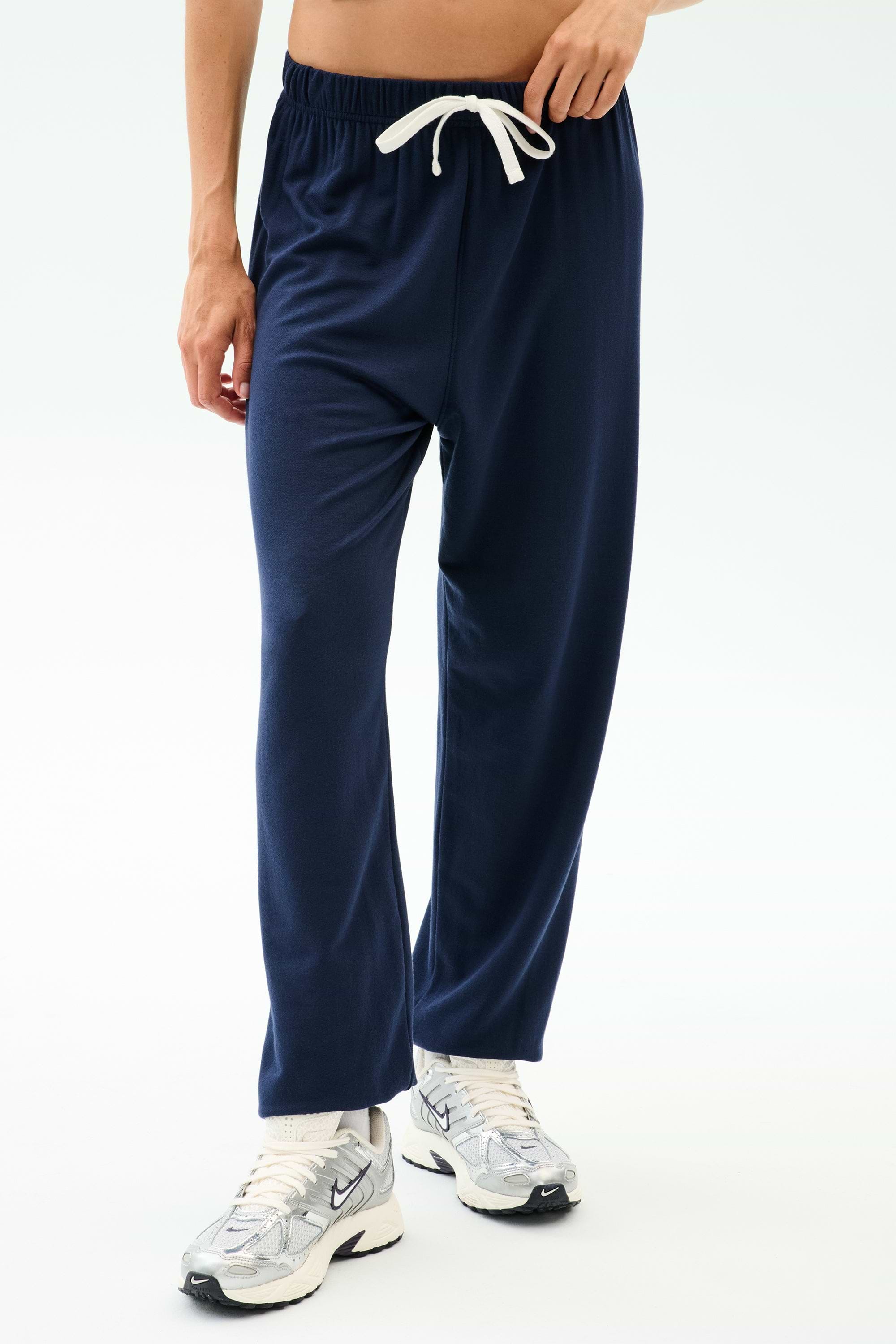 A person wearing SPLITS59's Andie Oversized Fleece Sweatpant in Indigo and white athletic shoes, pictured from waist to feet against a plain background.