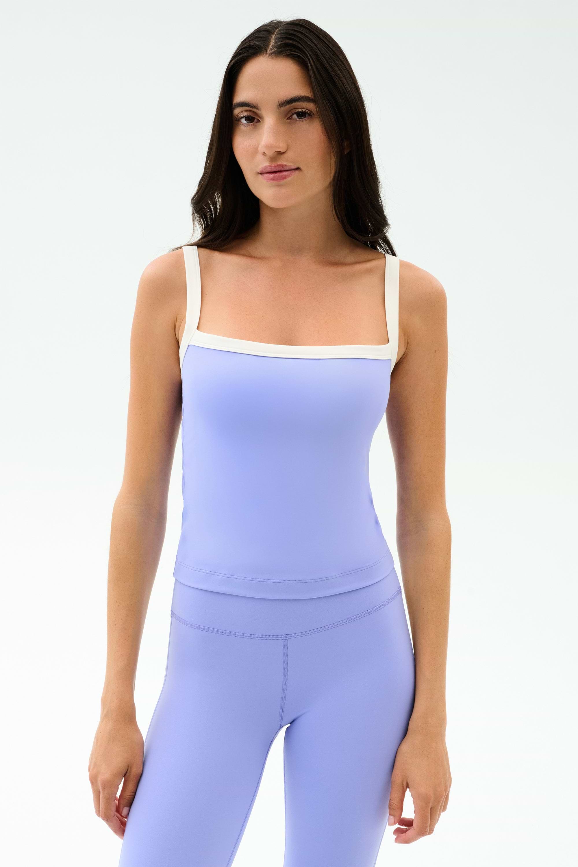 A woman faces forward in a fitted SPLITS59 Monah Rigor Tank in Purple Haze/White with matching leggings, set against a plain white background.