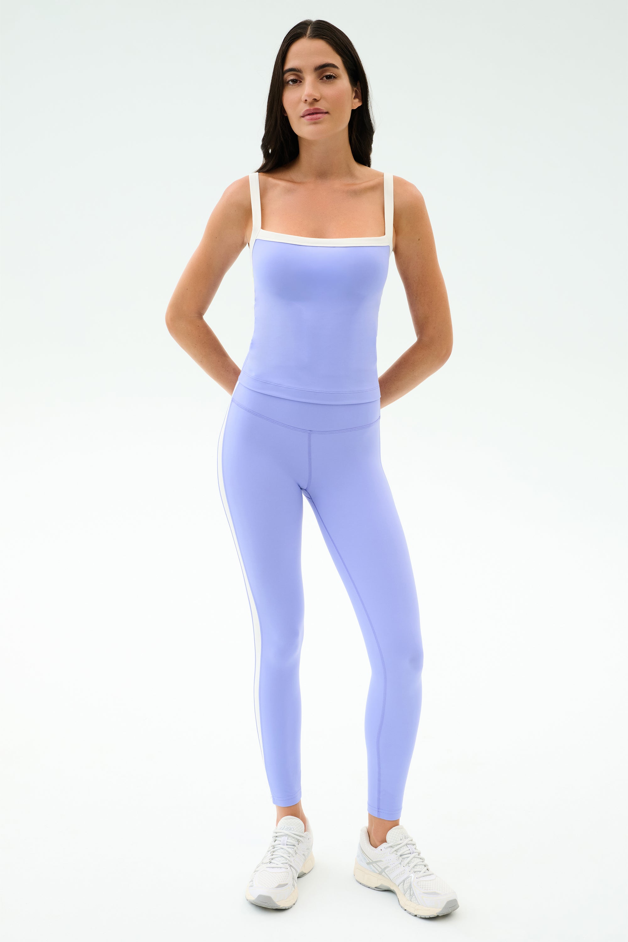 A person faces forward in SPLITS59 Clare High Waist Rigor 7/8 leggings in Purple Haze/White, paired with white sneakers, ready for the gym against a plain light background.