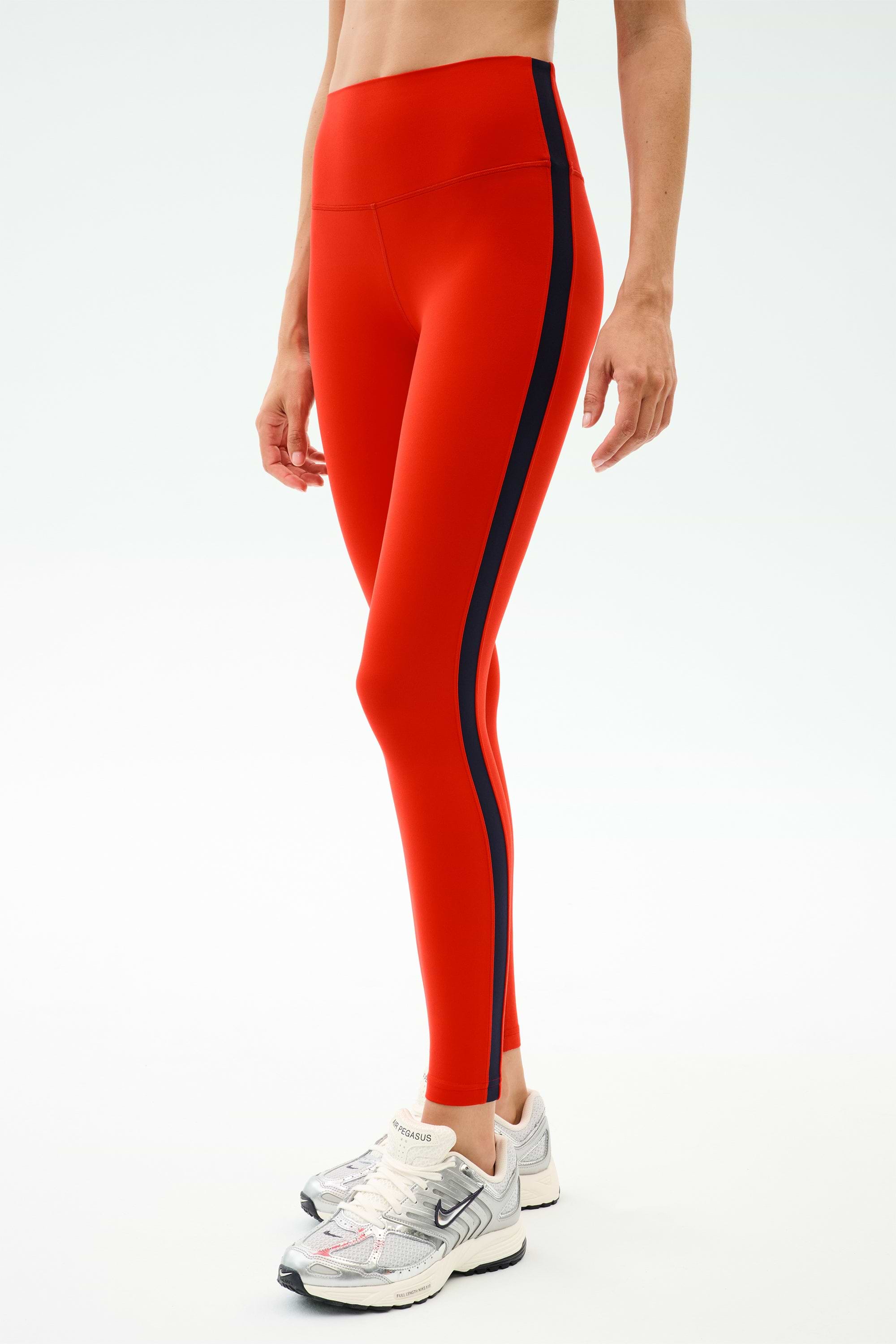 Person wearing SPLITS59 Clare High Waist Rigor 7/8 leggings in Lotus Red/Indigo, featuring a striking high waist and indigo side stripe—ideal for gym workouts or making a stylish statement.