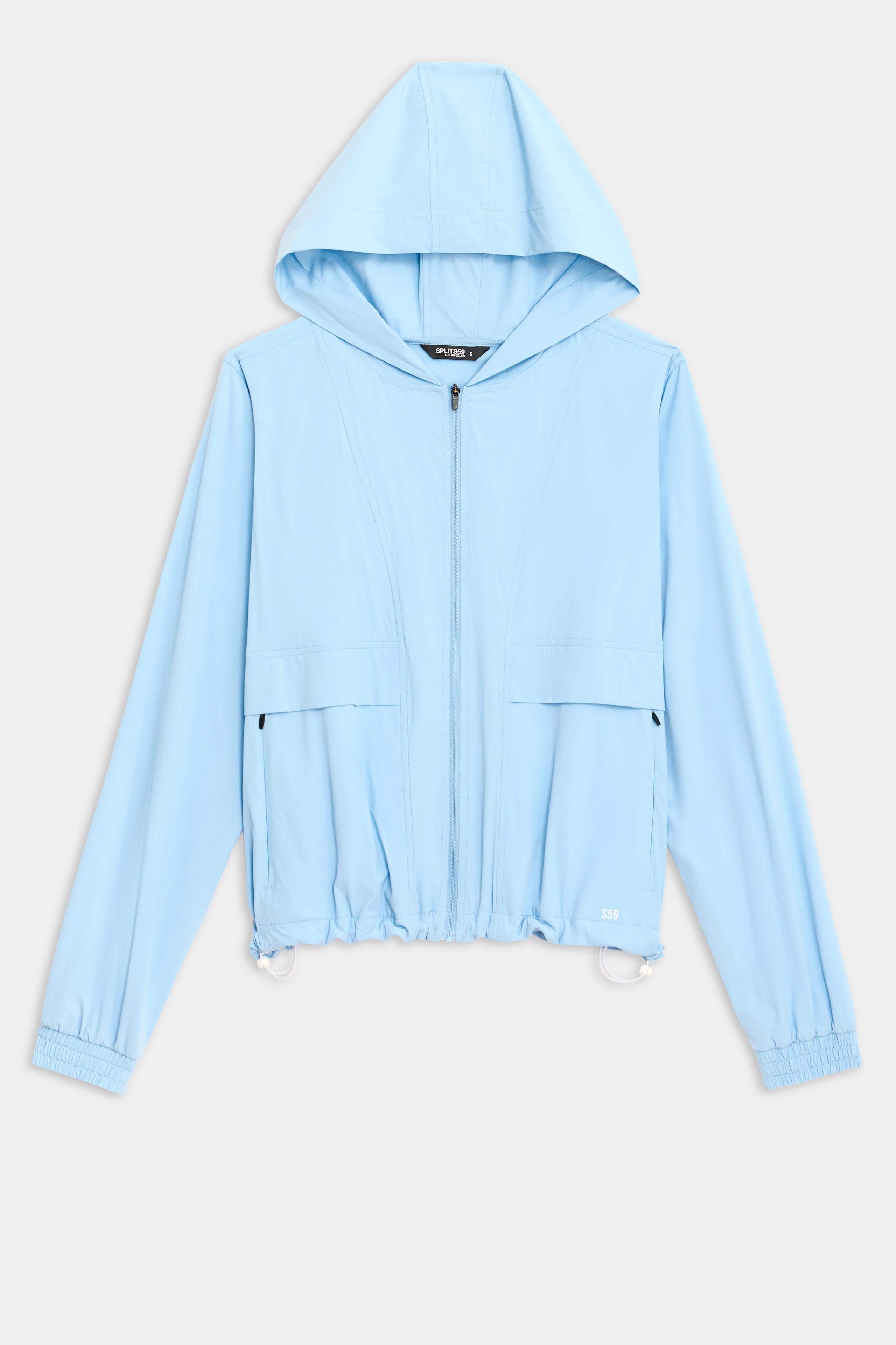 The Megan Woven Nylon Jacket by SPLITS59 is light blue with a hood, front zipper, two chest pockets, and elastic cuffs. It has a drawstring hem with adjustable toggles and is displayed on a plain white background.