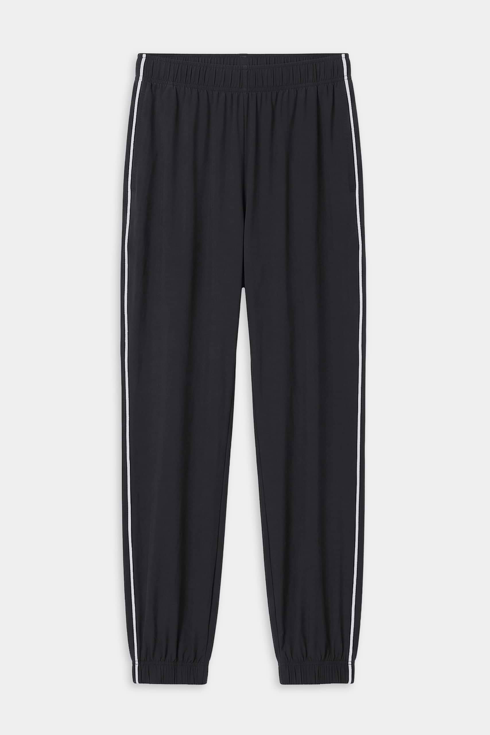 The SPLITS59 Megan Woven Nylon Jogger w/ Piping in black/creme features an elastic waistband and cuffs, white piping down each leg, and is made from an 85% nylon blend. Shown on a plain white background.
