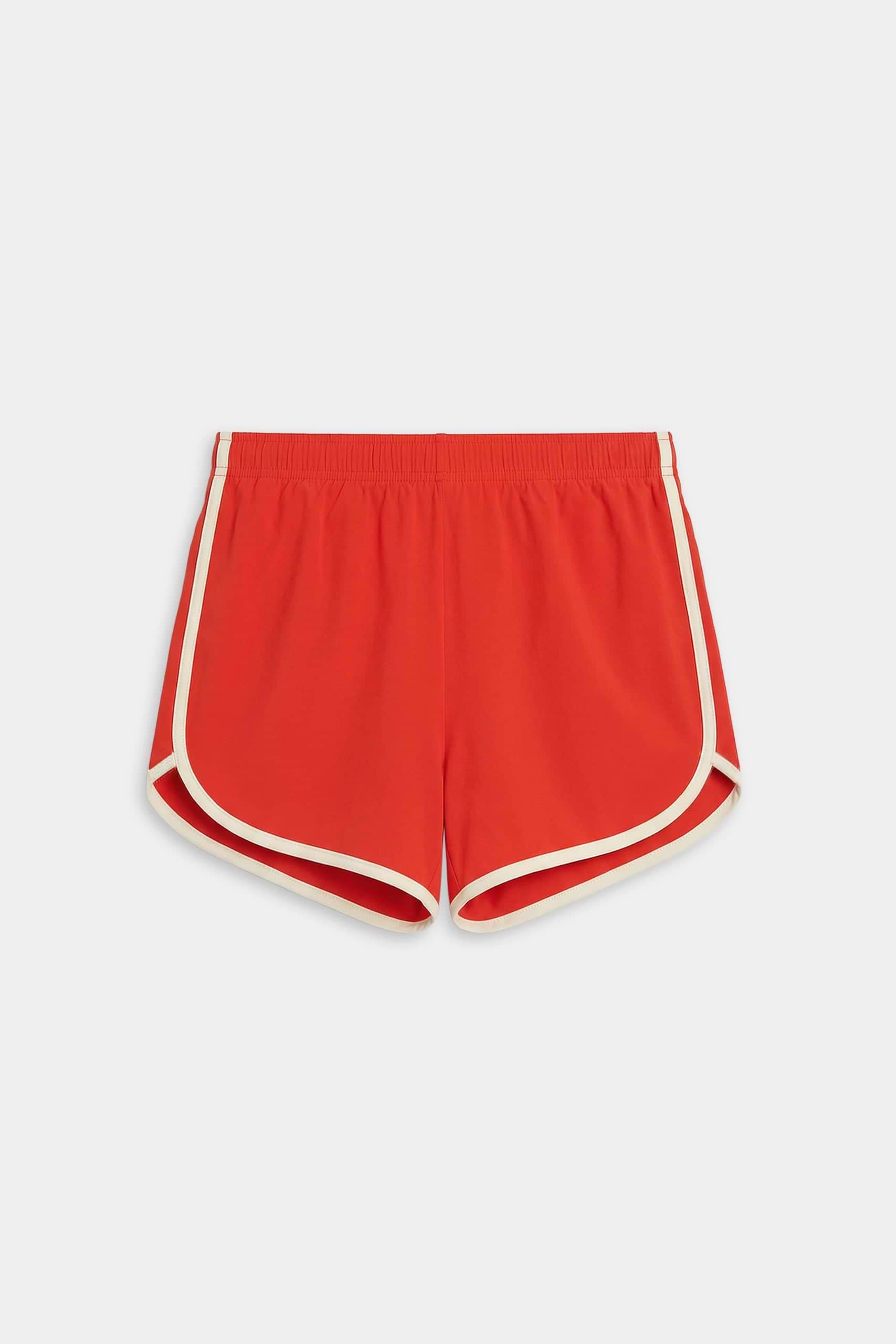 The SPLITS59 Megan Woven Nylon Run Short in Lotus Red/Creme features white piping and an elastic waistband, made from a nylon-spandex blend. Displayed against a plain white background.