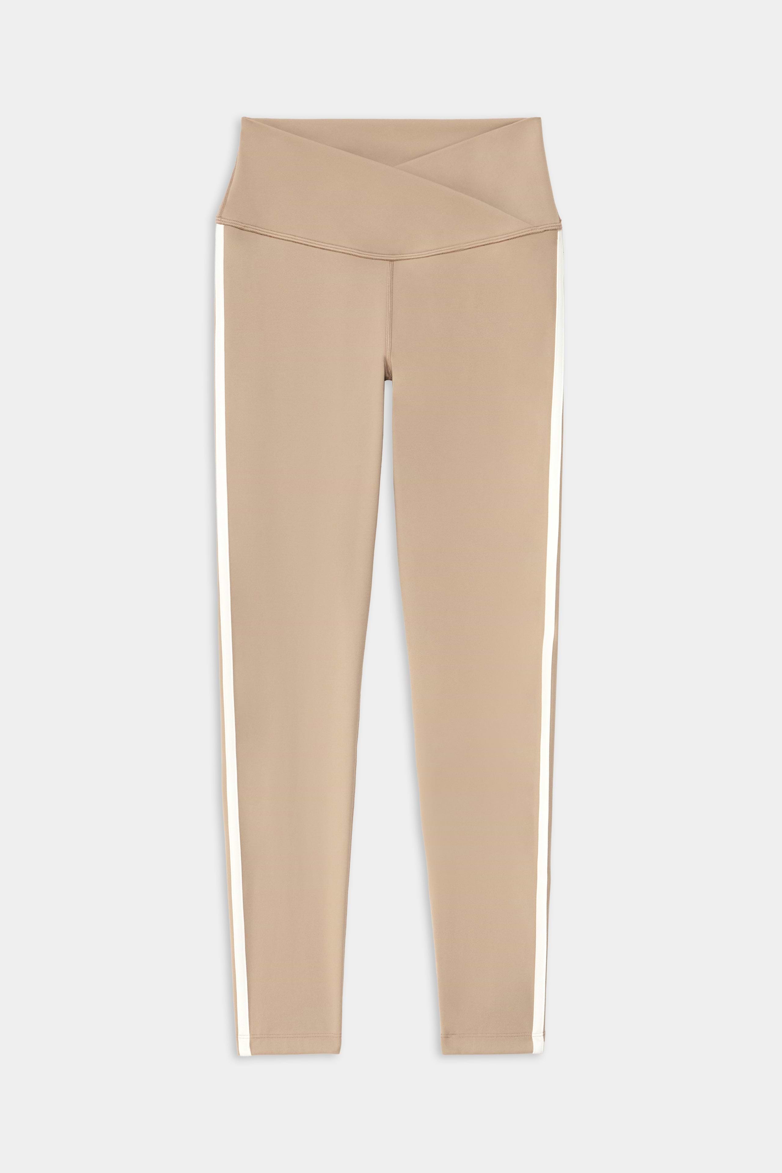 The SPLITS59 Mia Rigor Legging w/ Stripe in Latte/White features a high-waisted crisscross waistband, nylon blend fabric, and white vertical side stripes, shown laid flat on a white background.