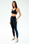 A woman models the SPLITS59 Ella High Waist Airweight 7/8 Black/Classic Blue leggings with a matching black sports bra and white sneakers, standing against a plain white background.