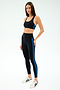 A woman wears the SPLITS59 Ella Airweight Bra in Black/Classic Blue, crafted from soft nylon spandex, paired with matching leggings and white sneakers, standing against a plain white background.