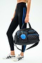 Wearing black leggings with blue stripes and white sneakers, a person carries the SPLITS59 MZW x Splits59 Duffle—a quilted black bag with blue accents and a round blue and red keychain.