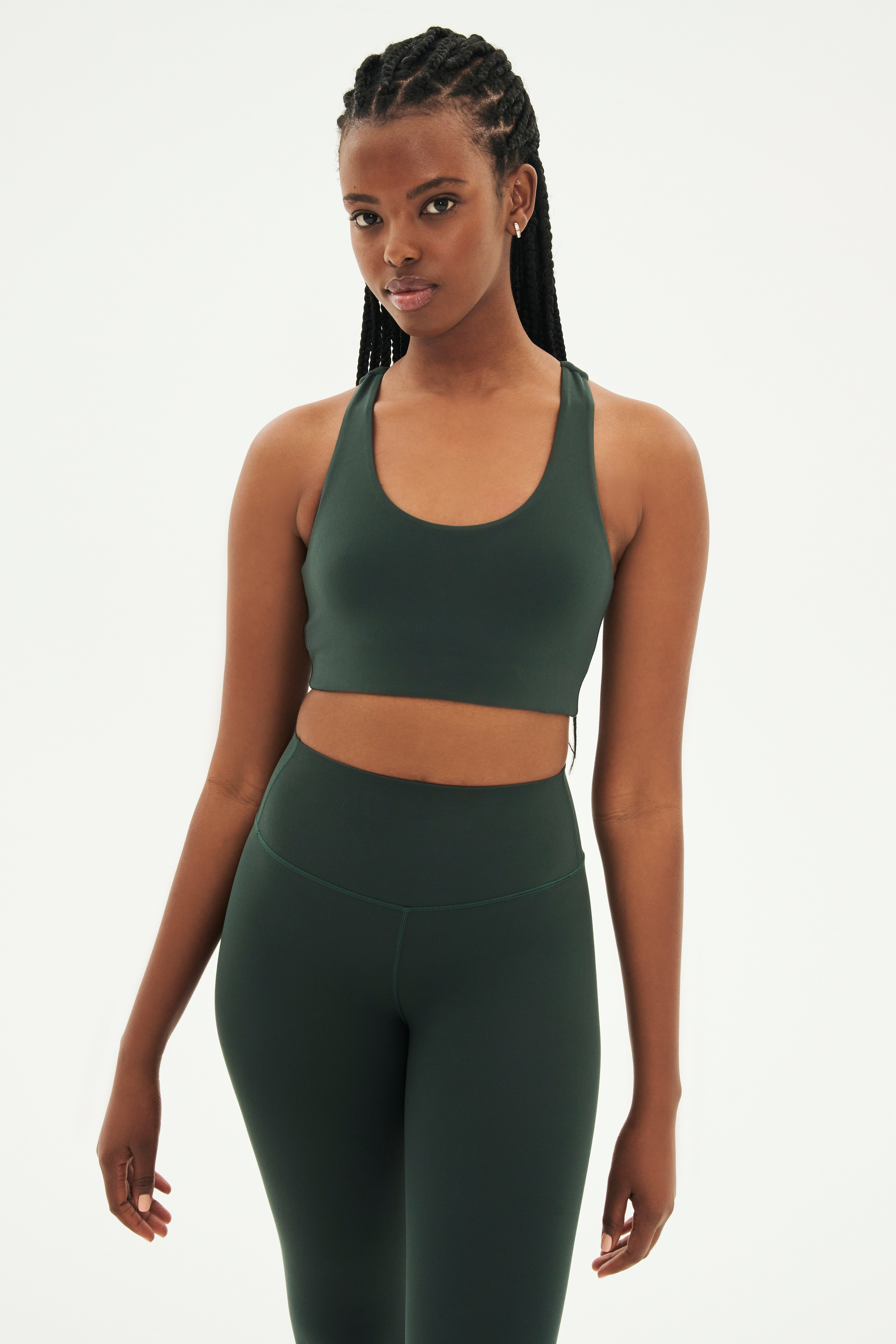 Front view of woman with black braids wearing dark green leggings and dark green bra