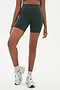 Front view of girl wearing highwaisted mid thigh dark dark green bike shorts with white shoes