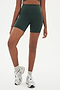 Front view of girl wearing highwaisted mid thigh dark dark green bike shorts with white shoes