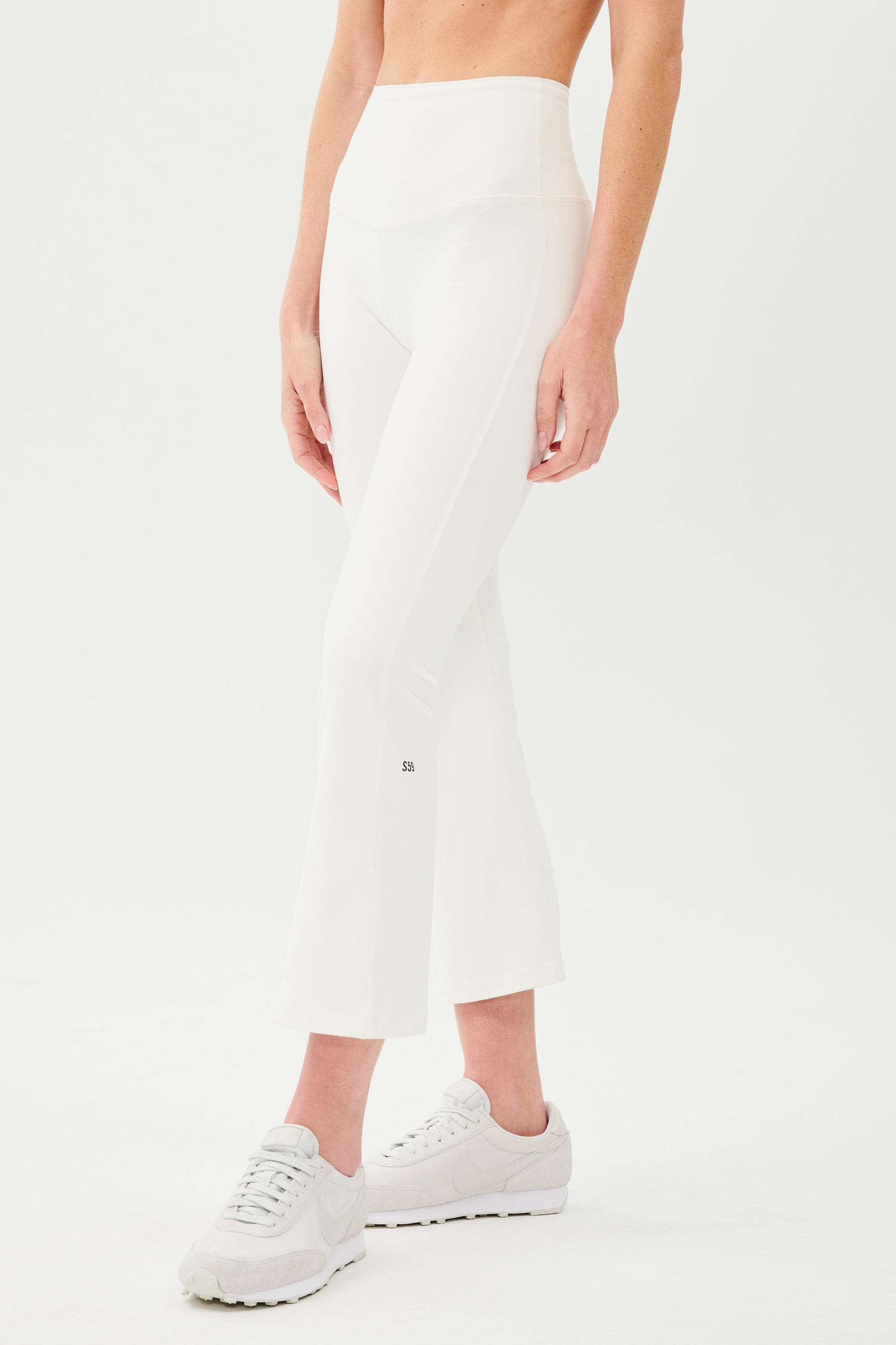 A woman wearing SPLITS59's Raquel High Waist Crop - White pant and white sneakers.