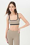 Front view of girl wearing dark light brown sports bra with black colored stripe along the ribs and black hem around the arms and neck with dark light brown leggings with two black stripes down the side