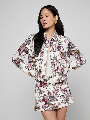 A woman wears the Nyx Cropped Jacket, a lightweight printed cotton piece paired with a matching skirt, standing against a plain light gray background and looking to the side with her hands on her waist.