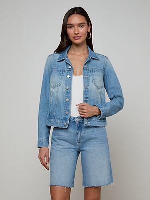 A woman with long dark hair and a neutral expression wears the Celine Jean Jacket in slim fit light denim wash over a white top, paired with matching knee-length light blue denim shorts, standing against a plain background.