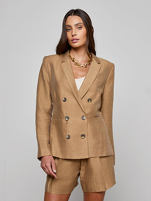 A woman poses against a light gray background wearing the Colin Linen-Blend Blazer in tan with matching tailored shorts, a white top, and a chunky gold chain necklace.
