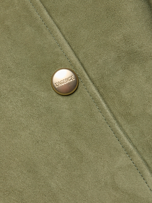 Close-up of light olive green suede from the Celina Suede Trench Coat, with a diagonal seam and round gold “LAGENCE” button—a timeless essential.