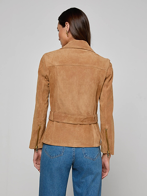 A woman with long brown hair stands with her back to the camera against a light background, wearing blue jeans and the Dinah Suede Biker Jacket in tan with gold zips and an adjustable belt.