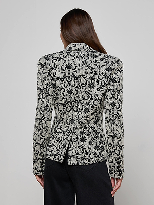 A person with long brown hair is seen from behind wearing the Bethany Flocked Tweed Blazer with a fitted waist and black-and-white pattern, paired with black pants, against a plain light background.