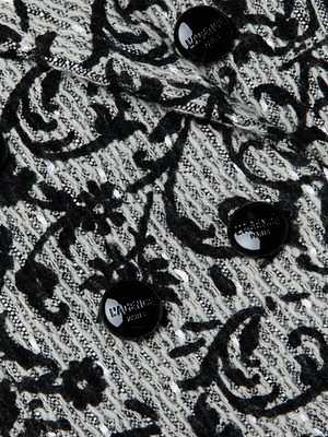 Close-up of a velvet-finish floral pattern on textured black and white fabric, accented by glossy black buttons—a luxe detail from the Bethany Flocked Tweed Blazer.
