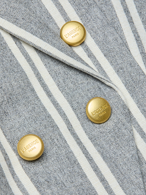 Close-up of the Kendi Longline Blazer, featuring gray and white striped Italian wool blend fabric and three gold L’AGENCE PARIS-engraved buttons arranged in two rows on its double-breasted front.