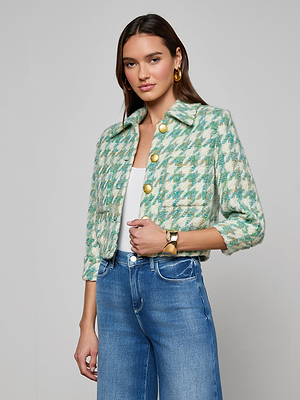 A woman models the Jia Houndstooth Tweed Jacket in jade green with gold buttons, styled with a white top, blue high-waisted jeans, gold hoop earrings, and a gold bracelet against a light gray backdrop.