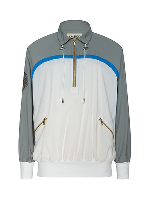 The Aurelia Windbreaker is a sporty, retro half-zip jacket featuring gray sleeves and top, white body, blue stripe accent, gold zippers, left sleeve patch, and a collar with white drawstrings for classic athleisure style.