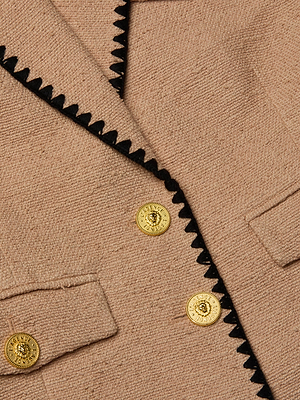 Close-up of the Wylla Tweed Blazer by L'AGENCE Sale in neutral tan, featuring black zigzag trim on the lapel, three gold decorative buttons, and a peek at two front pockets that showcase the blazer's refined, structured details.