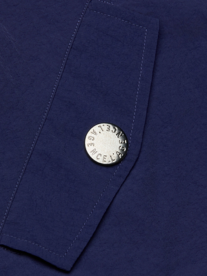 A close-up of a navy blue fabric pocket on the Geovana Hooded Windbreaker, featuring a large round silver button embossed with STELLA MCCARTNEY—a stylish travel essential.