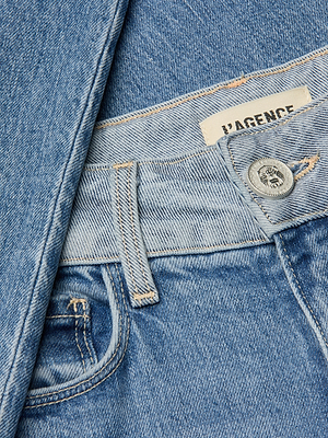 Close-up of blue Louane Wide-Leg Flare Jean made from stretch denim, featuring a visible button, belt loop, front pocket, and sewn-in VAGENCE label. A matching denim jacket is partially draped over the wide-leg jean.