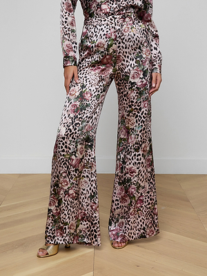 A person stands on a wooden floor wearing the Pilar Silk Wide-Leg Pant featuring a pink rose cheetah print, paired with open-toe gold heels.