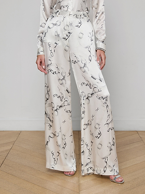 A person models the Gavin Silk Wide-Leg Pant in high-rise, white silk charmeuse with a black abstract print, standing on a wooden floor. Only their torso and legs are shown, hands at their sides.