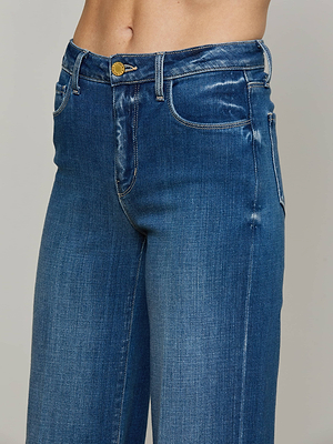 Close-up of a person wearing L'AGENCE Clayton Wide-Leg Jean, featuring high-rise blue denim, a gold button, visible front pockets, and belt loops; upper body and waistband shown against a plain background.