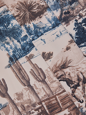 The Nova Pleated Wide-Leg Pant features a Western toile print with brown cacti, a galloping horse, wooden fences, and blue desert patchwork—perfect for standout suiting or wide-leg trousers.