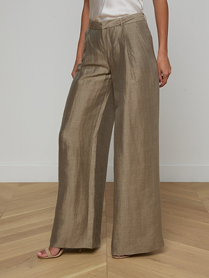 A person wearing the Allanah Linen-Blend Trouser in wide-leg, metallic taupe with a high waist and subtle sheen stands on a light wooden floor against a white wall; only the lower half of their body is visible.
