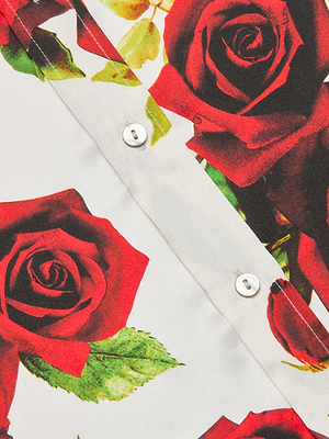 Close-up of the Dani Silk Blouse, a button-down made from silk, showcasing a bold red rose print with green leaves and white buttons along the center.