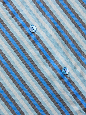 Close-up of the Tyler Silk Blouse by L'AGENCE, featuring diagonal blue, brown, and light gray stripes with two blue buttons on the seam.