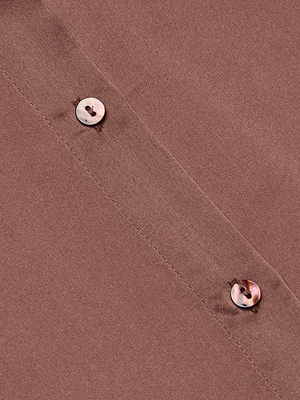 Close-up view of the Tyler Silk Blouse in mauve, showcasing two glossy buttons and visible stitching. The angled shot highlights the luxe texture and sheen of this long-sleeve button-down from L’AGENCE.